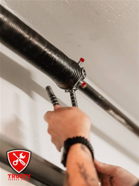 Technician winding a garage door torsion spring with winding bars in Plano, TX