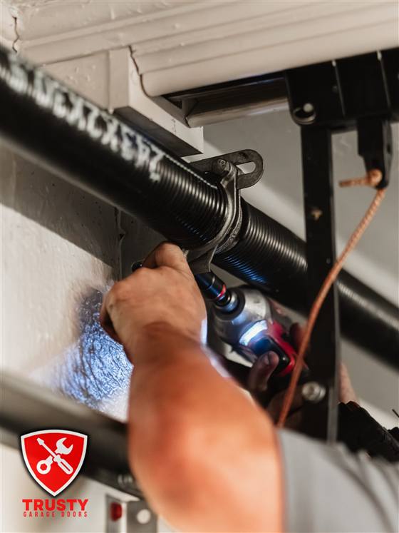 Technician tensioning a garage door torsion spring with an impact wrench in Dallas, TX